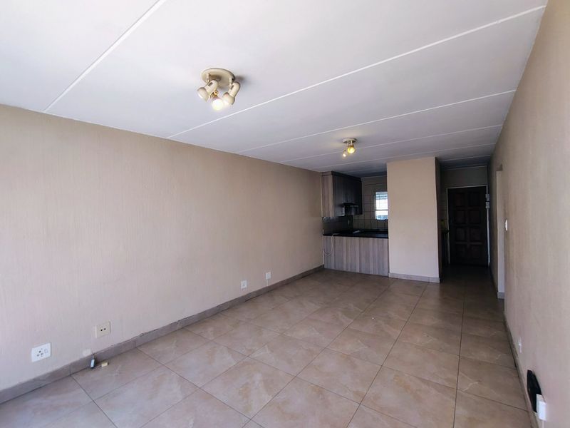 An open-plan living area featuring tiled flooring and a compact kitchen space with built-in cabinetry and countertops.