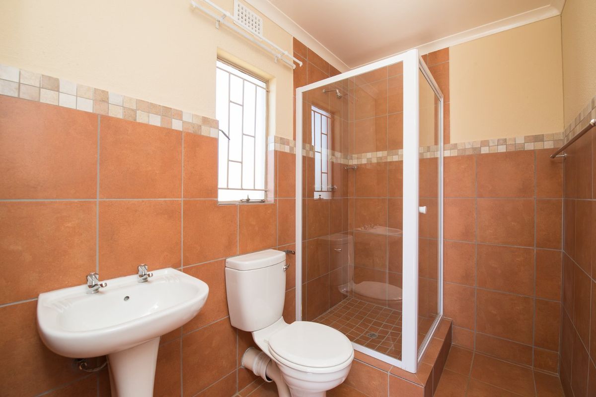 A functional bathroom featuring a pedestal basin, a toilet, and a glass-enclosed shower with terracotta-toned wall and floor tiling.