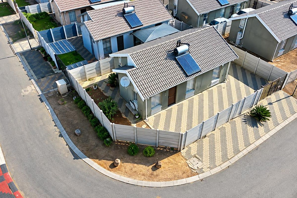 Aerial view of a residential property featuring a tiled roof with a solar water heater, paved driveway, and secure perimeter walling.