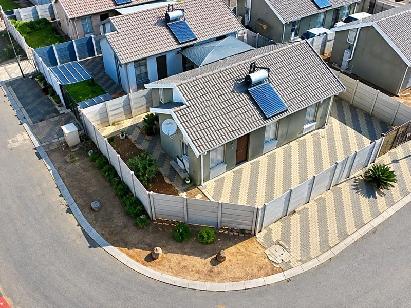 Aerial view of a residential property featuring a tiled roof with a solar water heater, paved driveway, and secure perimeter walling.