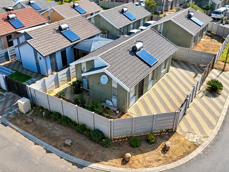 Aerial view of a residential property featuring a tiled roof with solar water heating, a paved driveway, and secure precast concrete boundary walls.