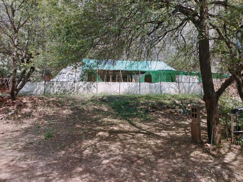 A rustic outdoor structure featuring a canvas tent-style enclosure with shade netting, situated in a wooded farm setting.