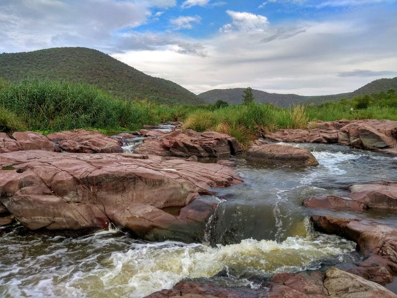 A scenic view of a natural stream flowing over rocky terrain, surrounded by lush vegetation and rolling hills on the farm property.