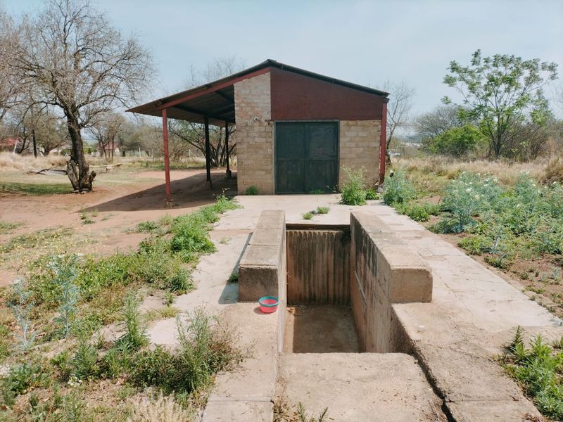 Outdoor utility area featuring a concrete inspection pit and a detached metal-framed shed structure on a farm property.