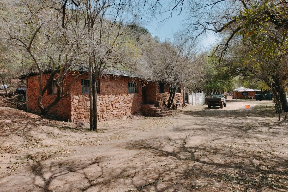 A rustic stone-built farm cottage set in a natural, wooded landscape with an unpaved approach.