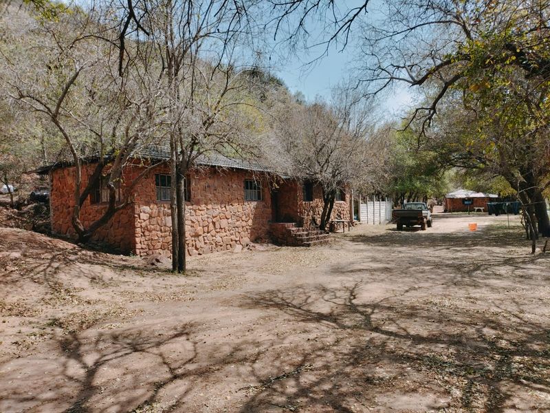 A rustic stone-built farm cottage set in a natural, wooded landscape with an unpaved approach.