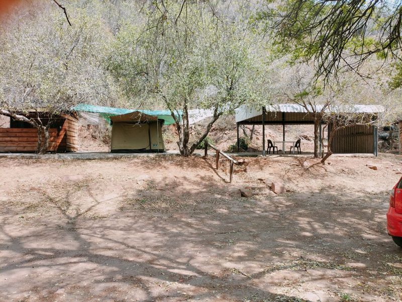 Outdoor recreational area featuring a concrete slab, covered patio structure with metal roofing, and timber-clad storage or utility space in a natural setting.