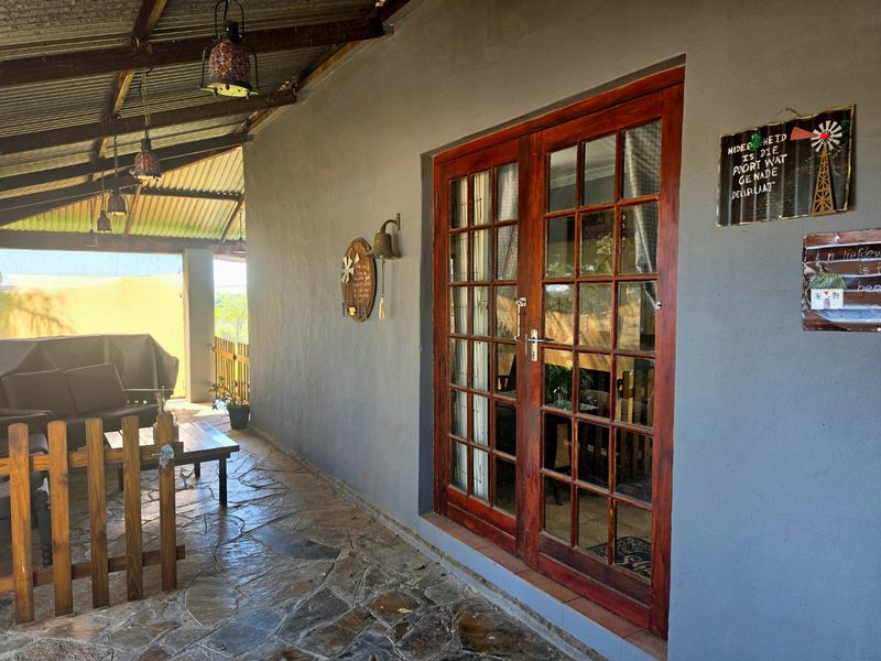 A covered patio area featuring rustic stone flooring, a corrugated iron roof, and wooden French doors leading into the home.