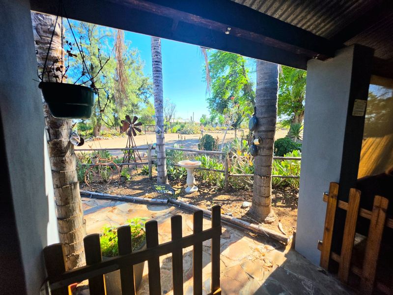 A covered patio area featuring stone flooring and timber fencing, overlooking a landscaped garden with mature trees and a rustic outdoor setting.