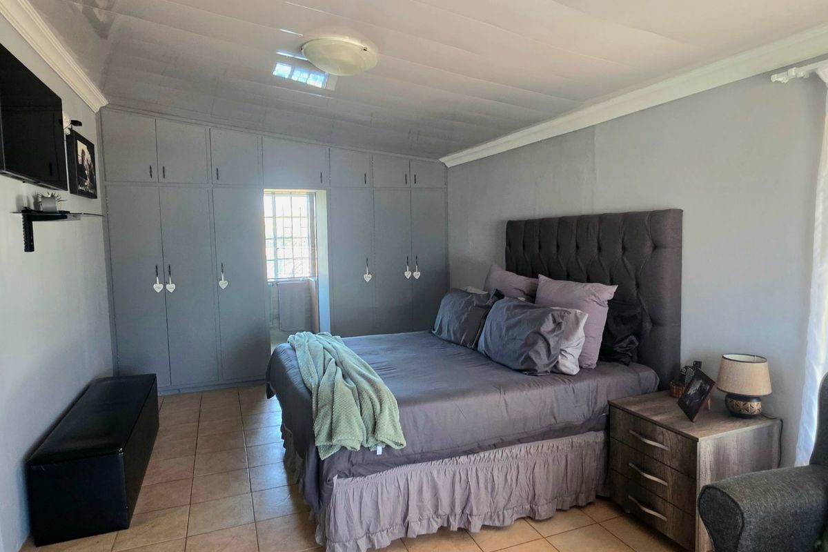 A spacious bedroom featuring extensive built-in cupboards, tiled flooring, and a neutral color palette, offering a functional and well-organized living space.