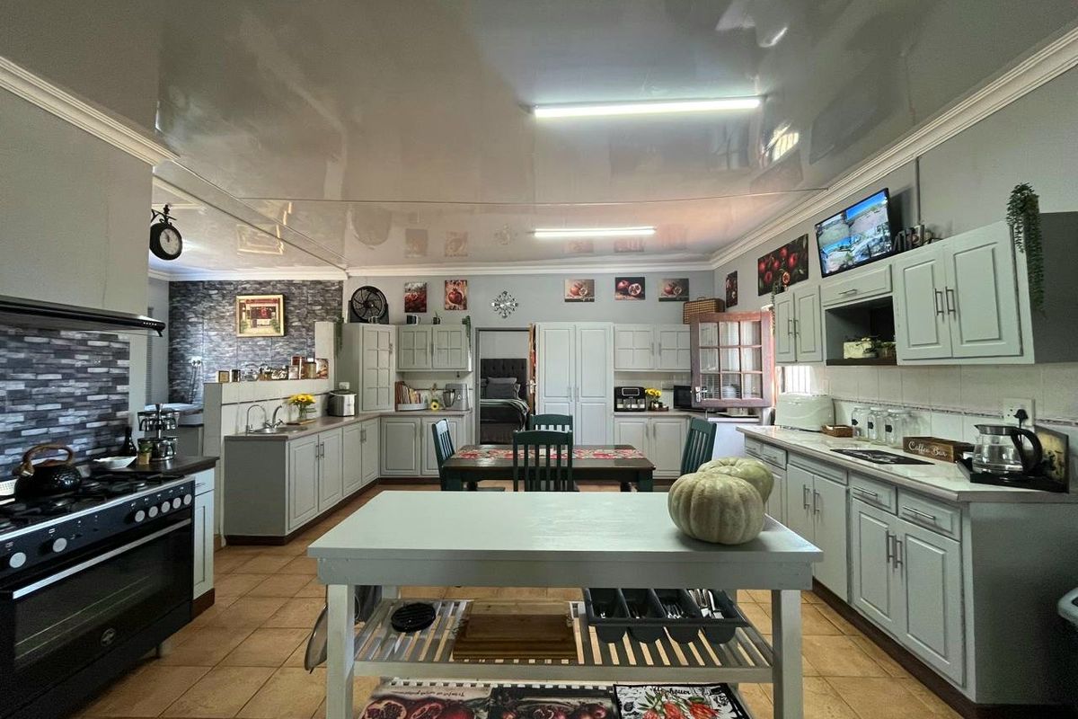 Spacious kitchen featuring extensive built-in cabinetry, a large gas stove with extractor, central island, and tiled flooring with a modern glossy ceiling finish.