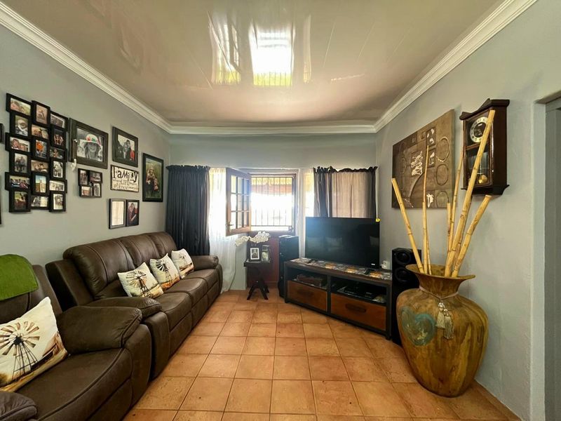 A comfortable living room featuring tiled flooring, a glossy ceiling with crown molding, and natural light through a casement window.