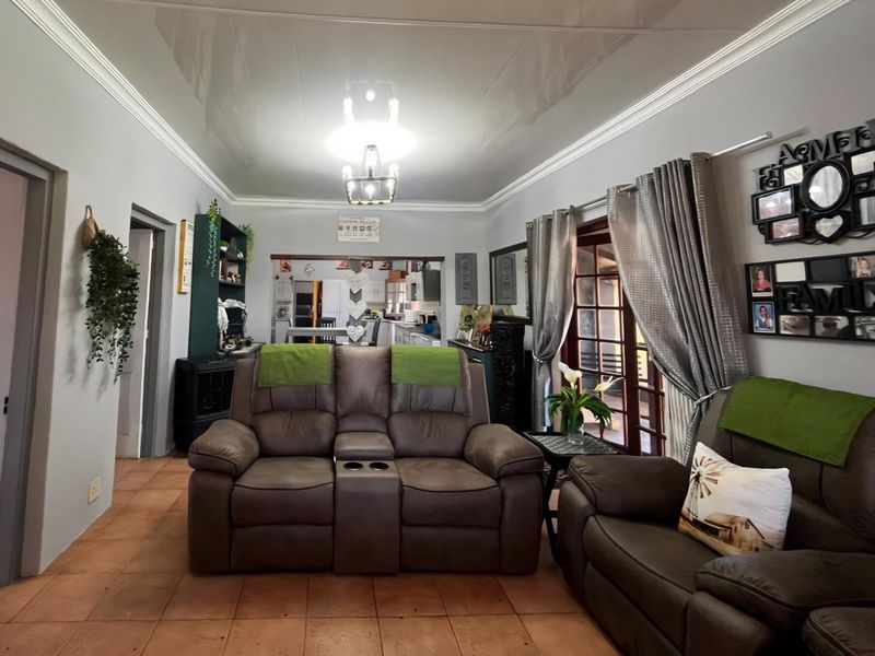 A comfortable living room featuring tiled flooring, crown molding, and a glossy ceiling, with direct access to an adjoining kitchen area.