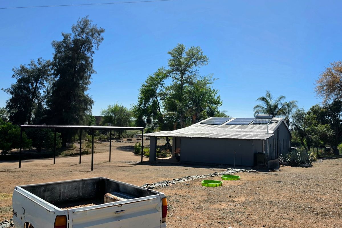 Rear view of the property featuring a corrugated metal roof with installed solar panels and a detached carport structure on a large plot.