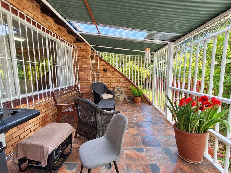 A covered outdoor patio featuring tiled flooring, brick wall accents, and a corrugated roof with translucent panels, providing a functional space for outdoor relaxation.