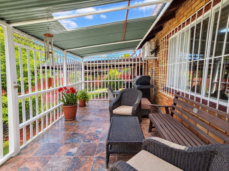 A covered outdoor patio area featuring tiled flooring, security bars, and a corrugated roof, providing a functional space for outdoor relaxation.