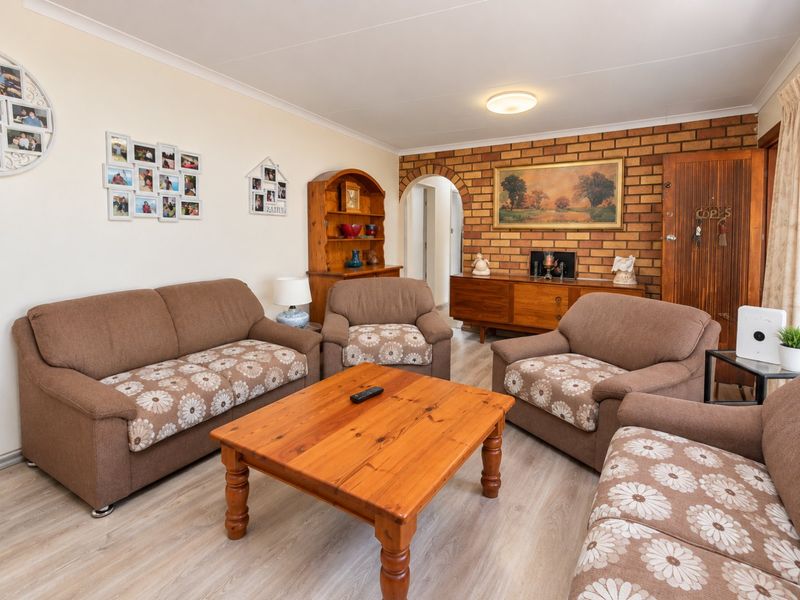 A comfortable living room featuring an exposed brick feature wall, arched doorway, and light-toned laminate flooring, offering a warm and traditional aesthetic.