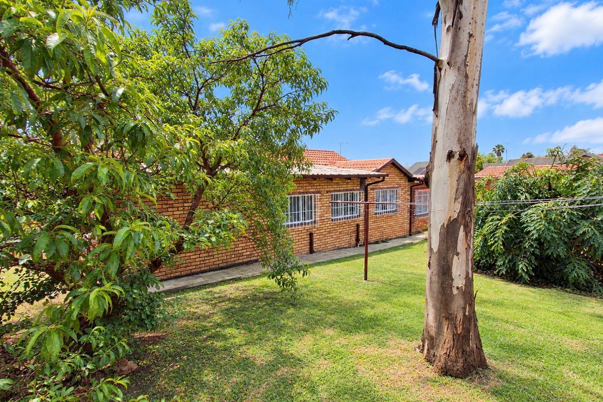 A view of the rear exterior of the house featuring a face brick facade, tiled roof, and security bars on the windows, set within a garden.