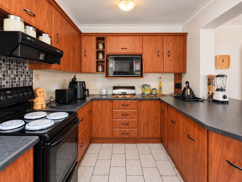 A functional U-shaped kitchen featuring warm-toned laminate cabinetry, dark countertops, tiled backsplash, and integrated appliances, offering a practical and well-maintained workspace.