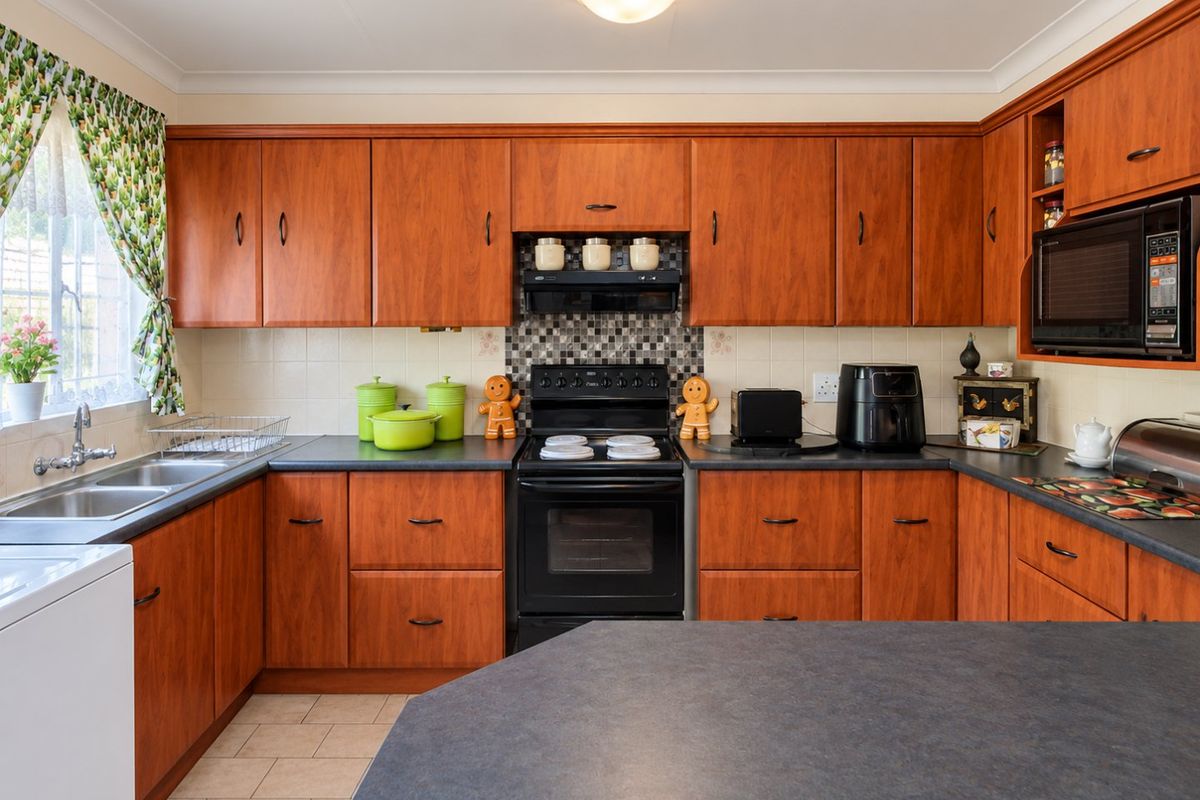 A functional kitchen featuring warm-toned wooden cabinetry, dark laminate countertops, a built-in oven with extractor fan, and a double basin sink.