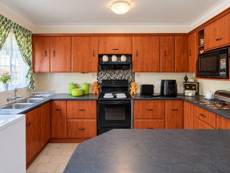 A functional kitchen featuring warm-toned wooden cabinetry, dark laminate countertops, a built-in oven with extractor fan, and a double basin sink.
