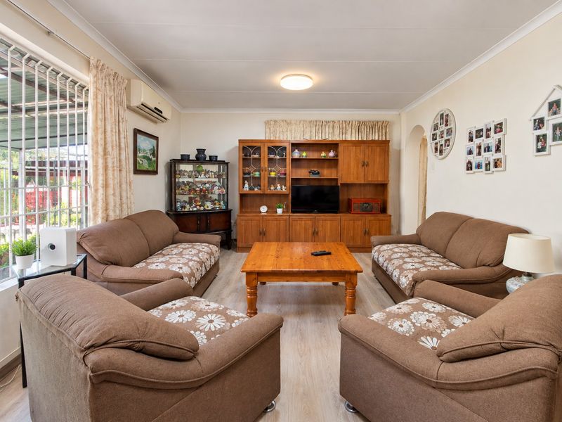 A comfortable living room featuring light-toned laminate flooring, a wall-mounted air conditioning unit, and large windows fitted with security bars.