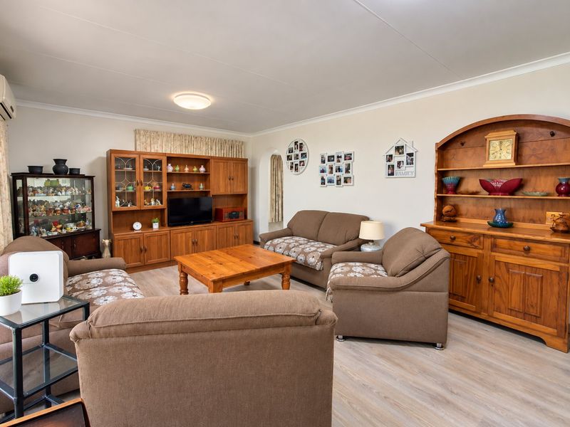 A comfortable living room featuring light-toned laminate flooring, coved ceilings, and an integrated air conditioning unit, providing a functional and well-maintained space.
