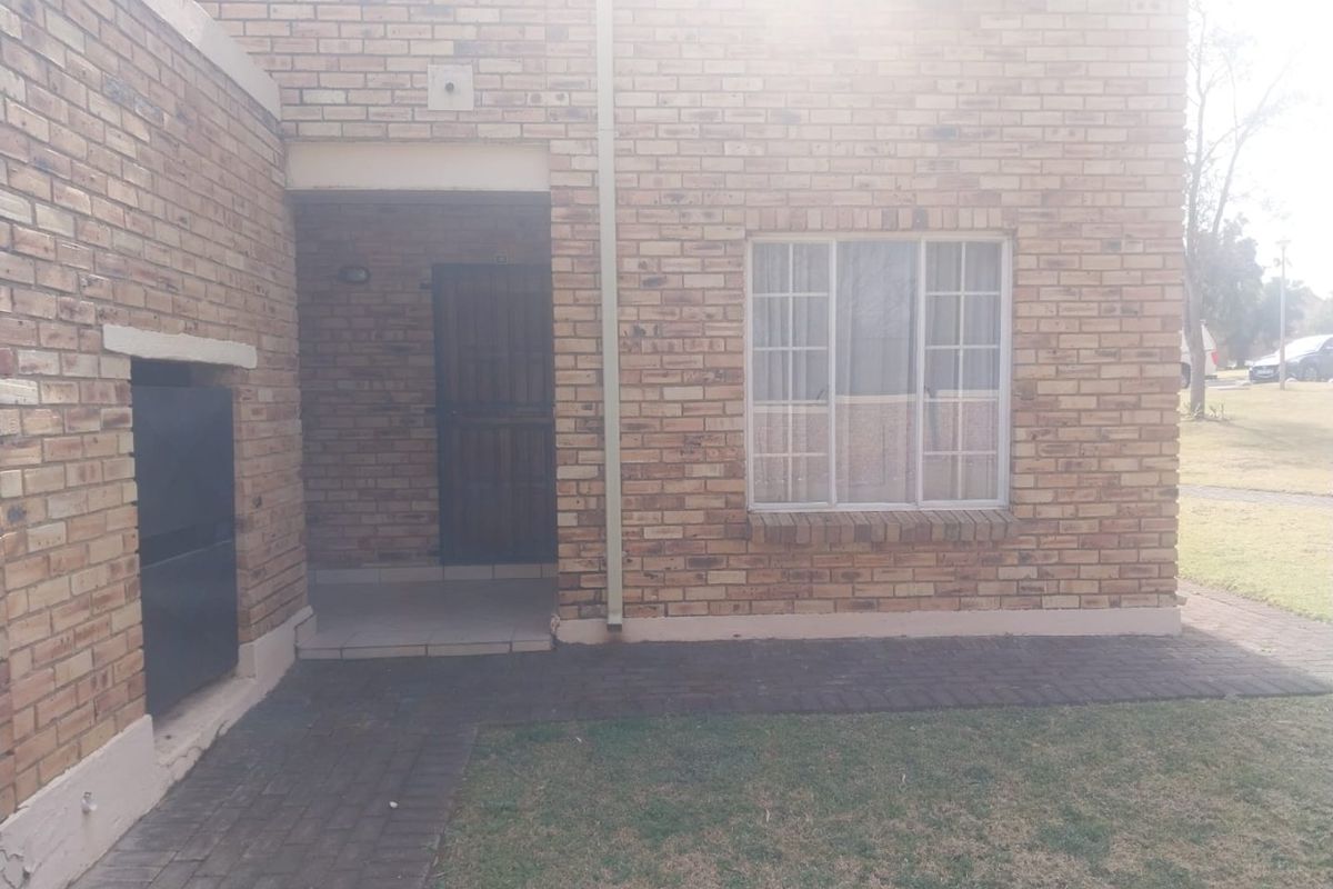 Rear exterior view of a face brick townhouse featuring a paved walkway, built-in braai area, and a small garden space.