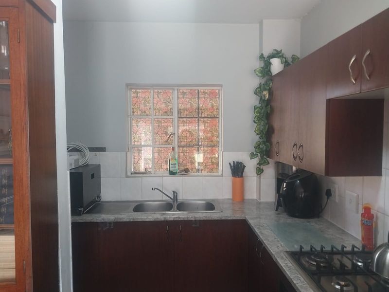 A functional kitchen featuring dark wood cabinetry, laminate countertops, a double bowl sink, and a gas hob with tiled splashback.