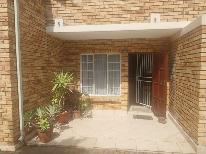 Front entrance of the townhouse featuring a brick facade, tiled patio area, and a secure timber door with a metal security gate.