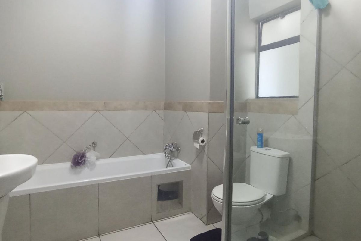 A functional bathroom featuring a bathtub, separate shower enclosure, pedestal basin, and toilet with neutral wall and floor tiling.