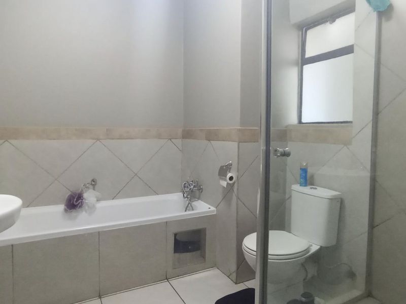 A functional bathroom featuring a bathtub, separate shower enclosure, pedestal basin, and toilet with neutral wall and floor tiling.