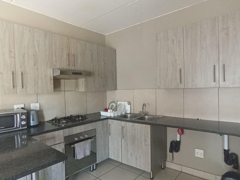 Functional kitchen featuring light wood-grain cabinetry, granite countertops, a gas hob, built-in oven, and tiled finishes throughout.