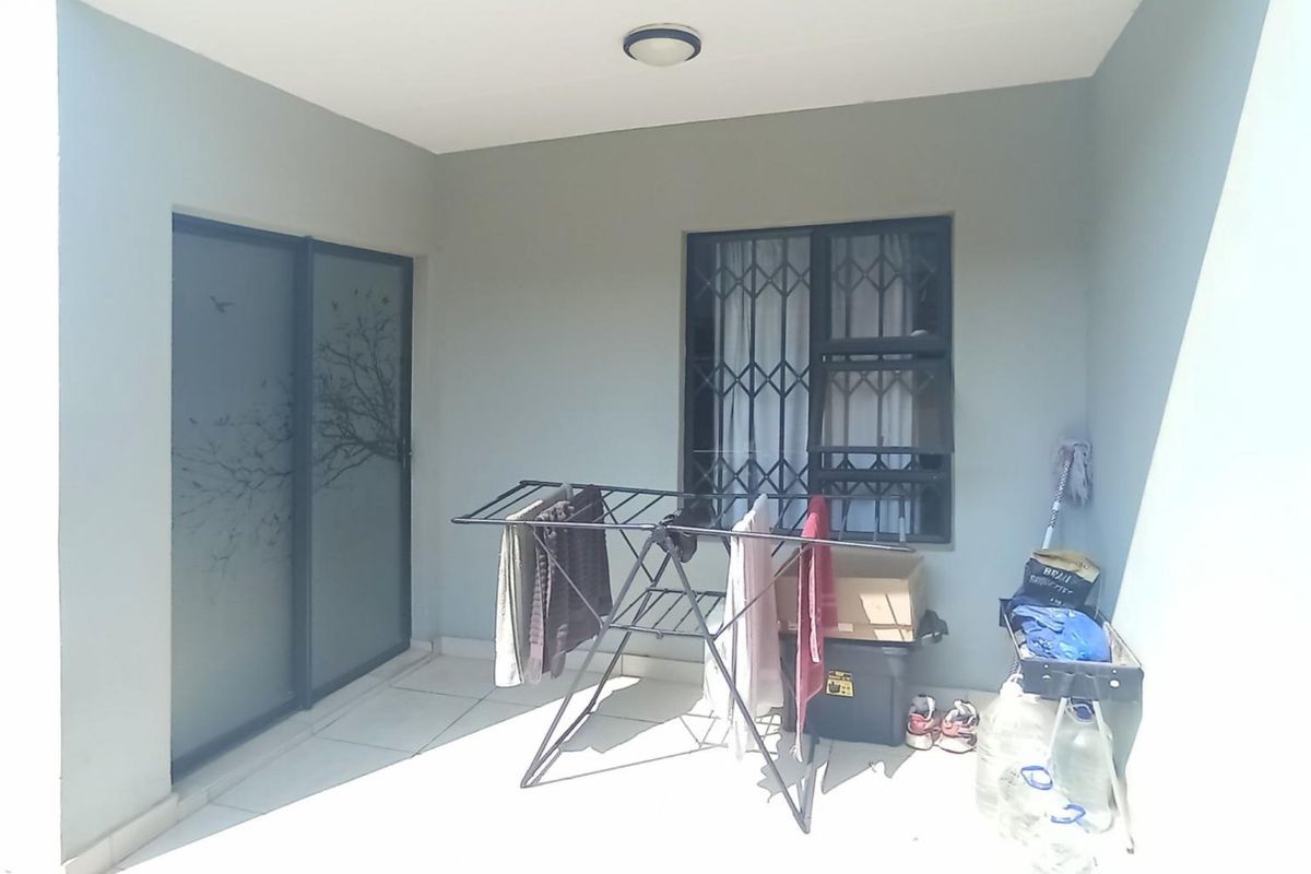 A covered patio area featuring tiled flooring, a sliding glass door, and a window with a security gate.