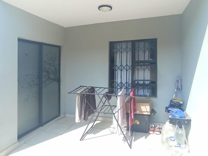 A covered patio area featuring tiled flooring, a sliding glass door, and a window with a security gate.