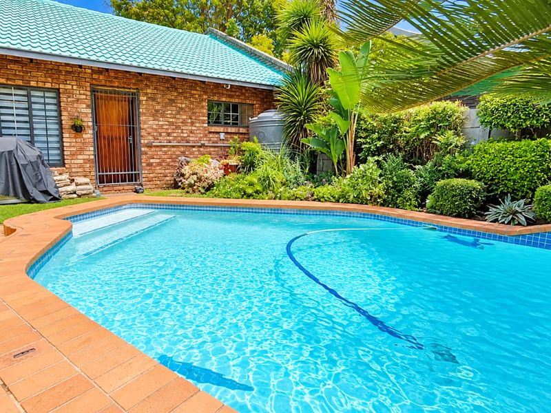 A well-maintained swimming pool area featuring a brick exterior facade, tiled roof, and established garden landscaping.