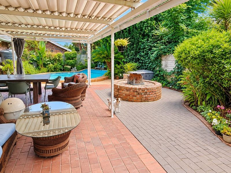 A spacious covered patio area featuring brick paving, a built-in brick fire pit, and direct access to an outdoor swimming pool.