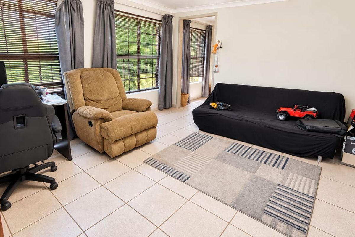A living room featuring neutral tiled flooring, large windows with venetian blinds, and classic cove cornicing, offering a functional and well-lit space.