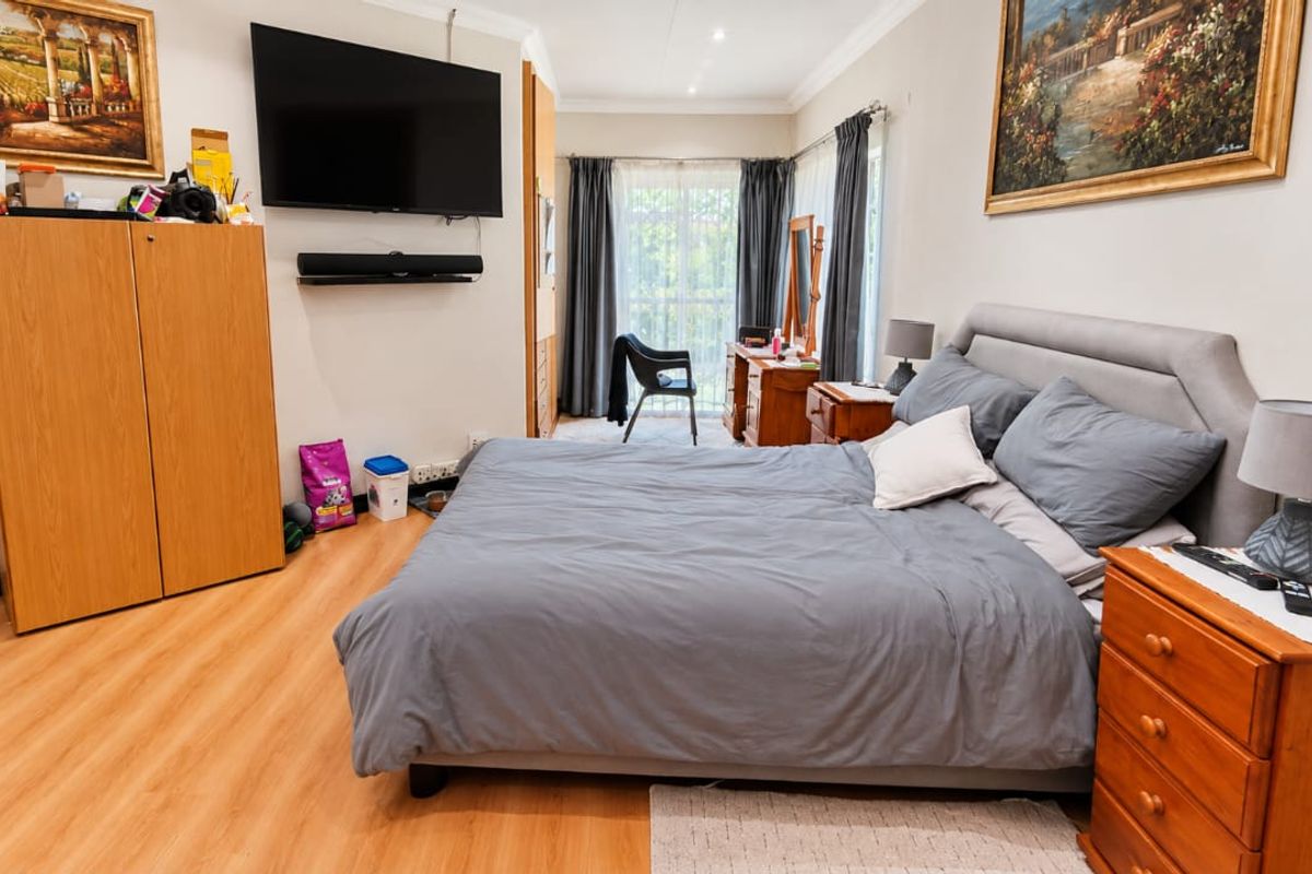 A well-lit bedroom featuring laminate flooring, built-in cupboards, and a sliding glass door providing access to the exterior.