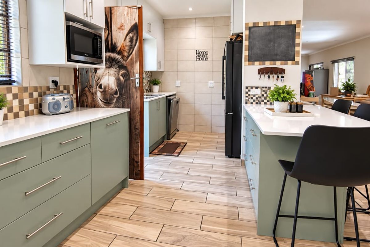 Modern kitchen featuring sage green cabinetry, white quartz countertops, a central island with breakfast bar seating, and neutral tiled flooring throughout.