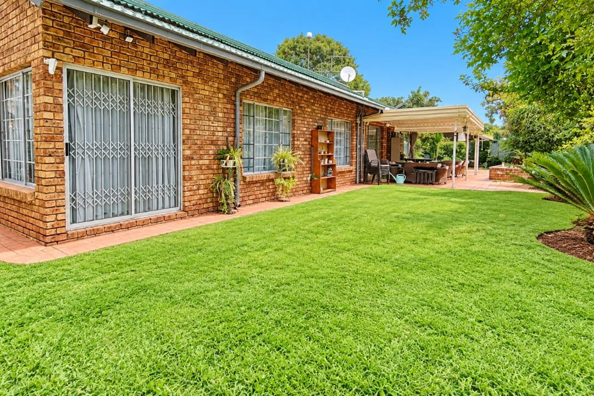 Rear view of the house featuring a face brick facade, sliding glass doors with security gates, a covered patio area, and a well-maintained lawn.