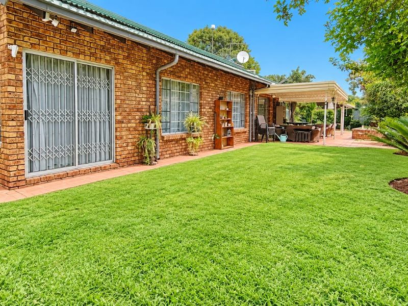 Rear view of the house featuring a face brick facade, sliding glass doors with security gates, a covered patio area, and a well-maintained lawn.
