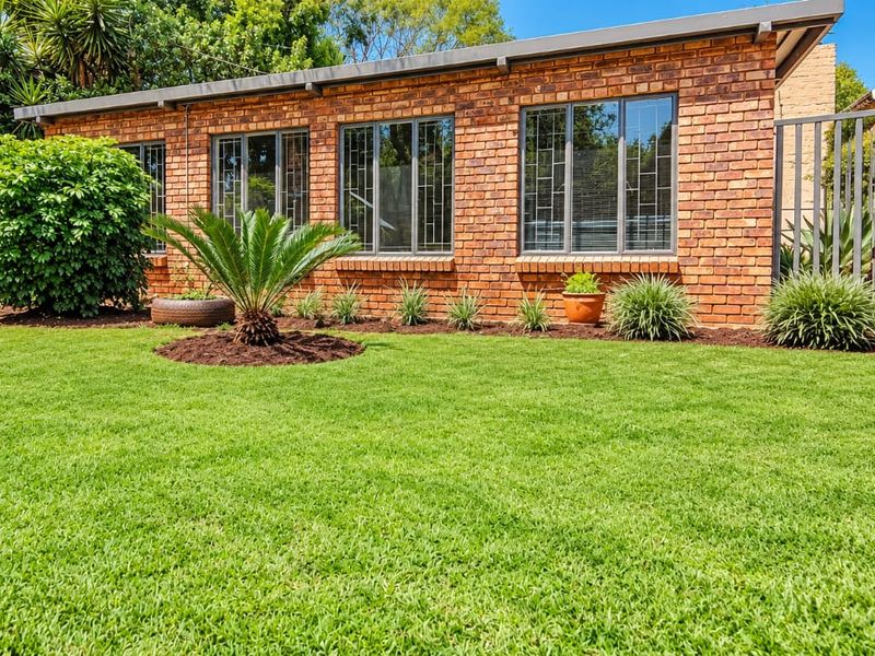 A well-maintained rear exterior view featuring a face brick facade, large aluminium windows with security bars, and a neatly landscaped lawn.