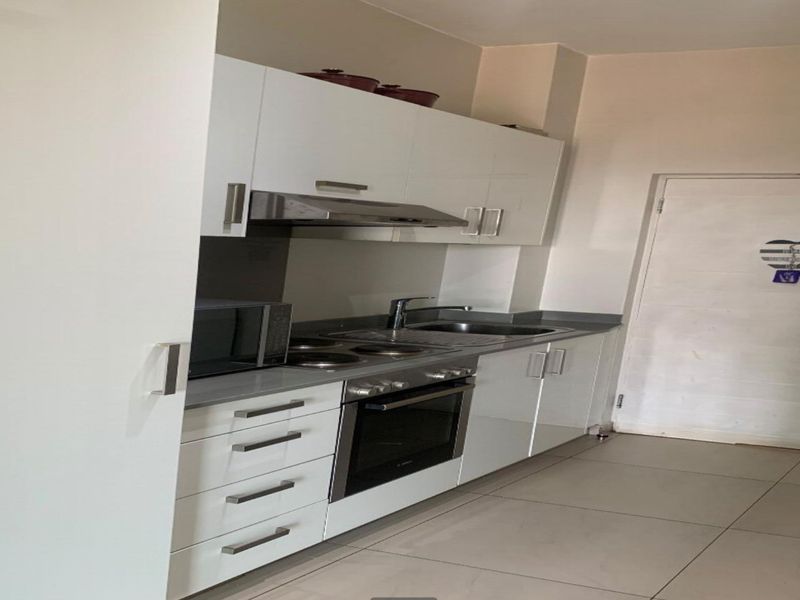 A modern kitchen featuring white cabinetry, stainless steel appliances including an oven and extractor fan, and neutral tiled flooring.