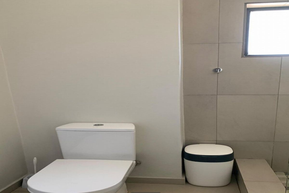 A clean, functional bathroom featuring a modern toilet, tiled shower area, and neutral wall finishes with natural light from a window.