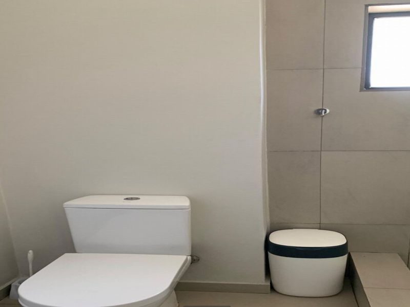 A clean, functional bathroom featuring a modern toilet, tiled shower area, and neutral wall finishes with natural light from a window.
