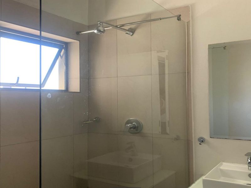 Modern bathroom featuring a glass-enclosed shower, contemporary basin, and wall-mounted mirror with neutral tiling.