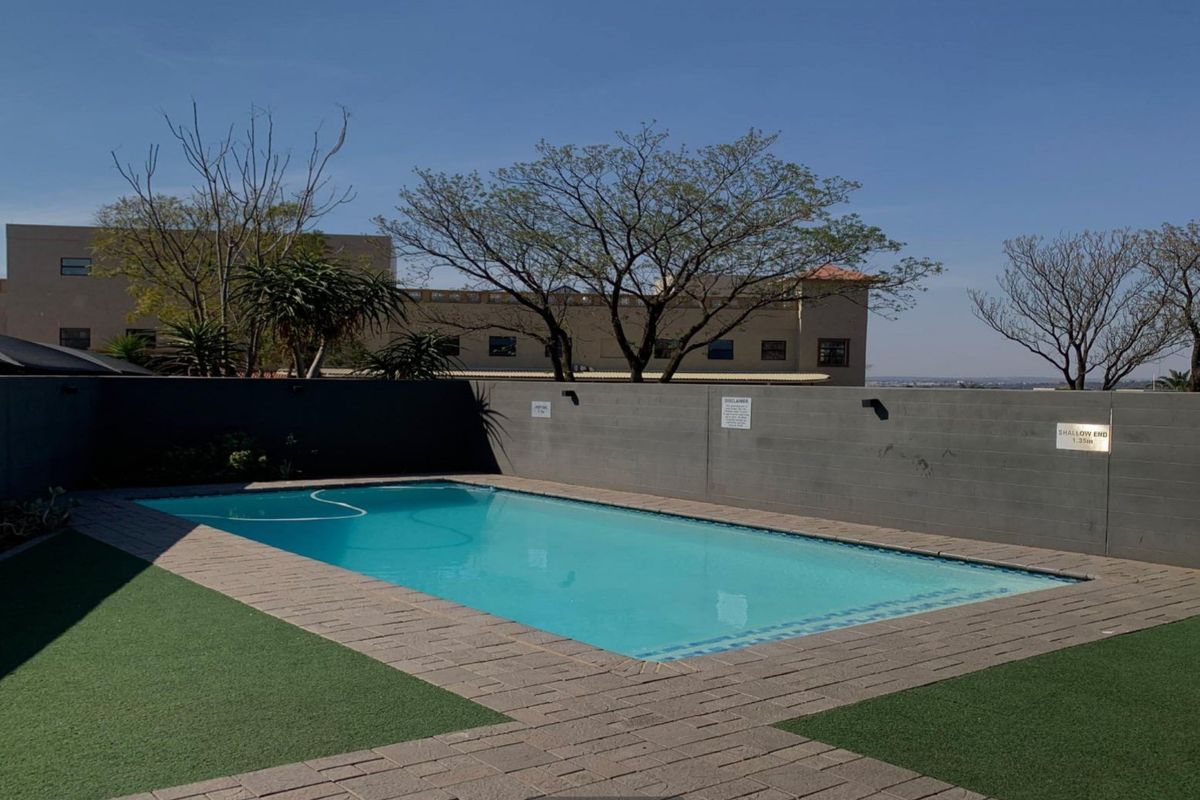 A well-maintained outdoor swimming pool area featuring a paved surround, artificial turf, and a private boundary wall.