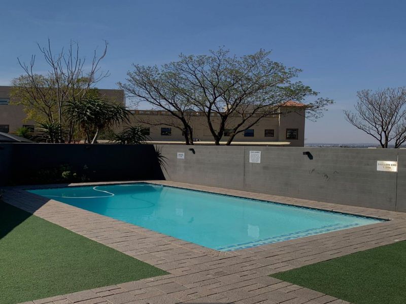 A well-maintained outdoor swimming pool area featuring a paved surround, artificial turf, and a private boundary wall.