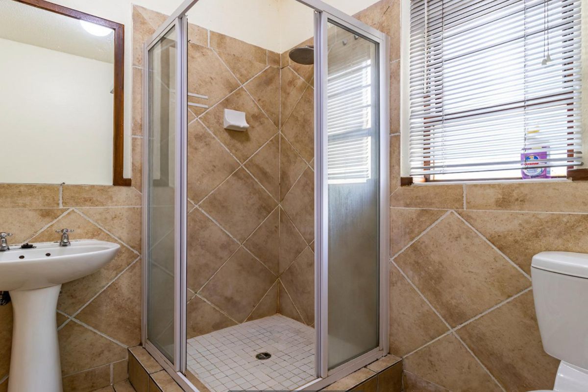 A functional bathroom featuring a pedestal basin, a glass-enclosed shower, and a toilet, finished with neutral-toned wall and floor tiles.